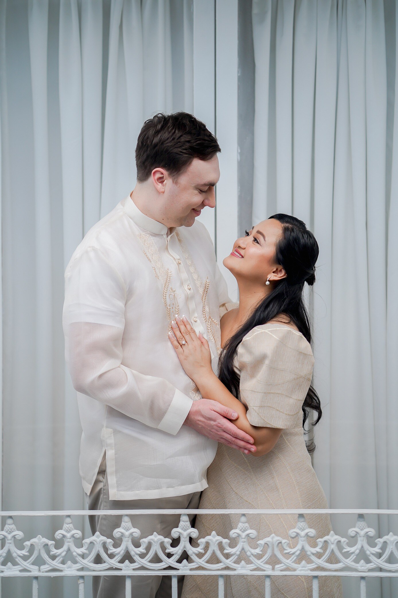 Michael in a barong and Winnie in a Filipiniana dress, smiling at each other